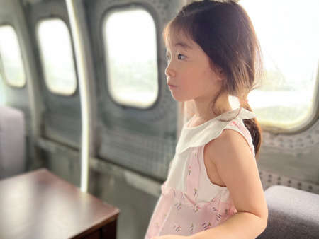 Beautiful little girl thoughtfully looks at the open space with copy space near the table, chair,...