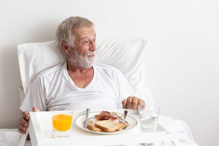 Senior retirement male has breakfast with orange juice and water on bedの写真素材