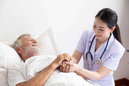 Nurse cares for elderly man lying in bedの写真素材