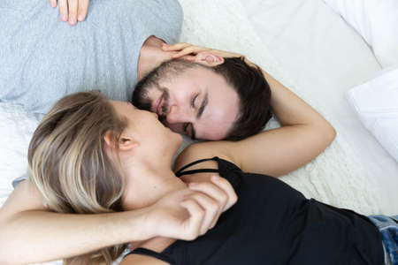 Lovely happy couple in love, smile, and kiss each other on their bed in the bedroomの写真素材