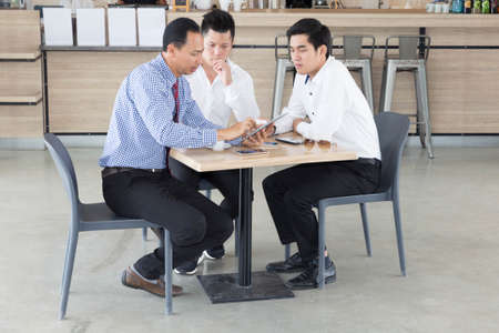 Three Asian businessmen discussing while having coffee together