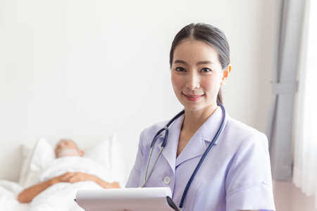 Young female nurse smile with medical record in front of a sleeping old man patientの写真素材
