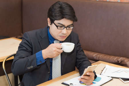 Asian businessman using mobilephone while drinking coffee in a coffee shopの写真素材