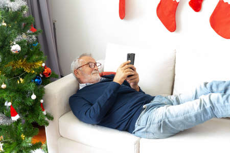Senior retirement male relax playing his mobile phone on sofa after decorate the chritmas tree
