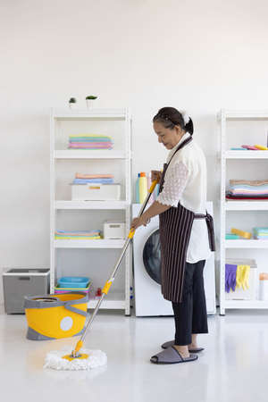 An elderly senior woman is happy cleaning a room floor alone using a mopの写真素材