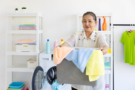 Senior woman with smile preparing to load dirty cloth in washing machine from laundry basketの写真素材