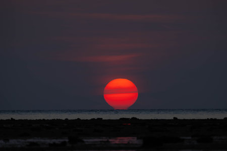 Closeup of bright big sun on the sky with yellow orange gradient colors during the sunset over the sea and beachの写真素材
