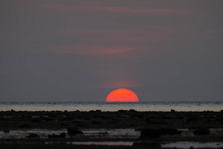 Closeup of bright big sun on the sky with yellow orange gradient colors during the sunset over the sea and beachの写真素材