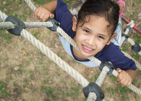 A cute girl is climbing on the rope ladder at public playgroundの写真素材