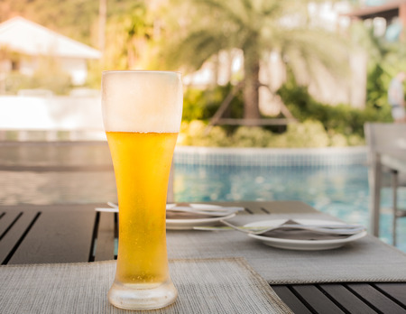 A glass of beer on the table under sunlight at swimming poolの写真素材