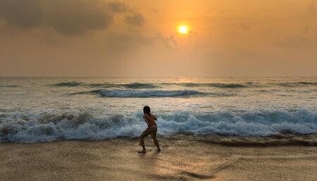 Little girl playing on the beach with strong wave during sunsetの写真素材