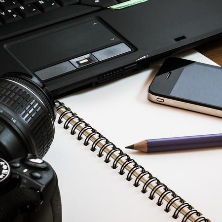 Pencil on notebook with camera, laptop and cell phone are on wooden tableの写真素材