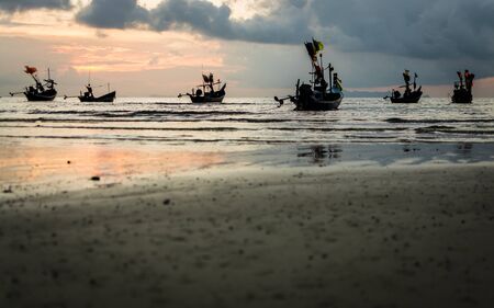 Many fishing boat in the sea when low tide during sunset