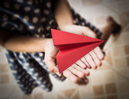 Little girl holding a red aircraft paper origami in her handsの写真素材