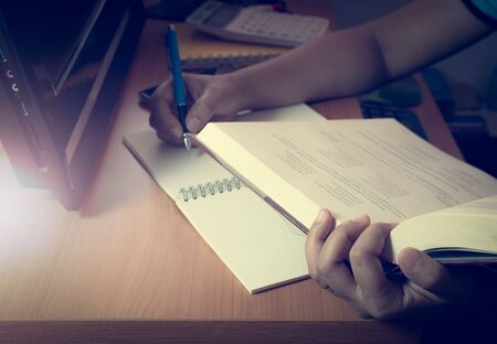 Hands of a girl doing homework on the desk with pc under shinning lightの写真素材