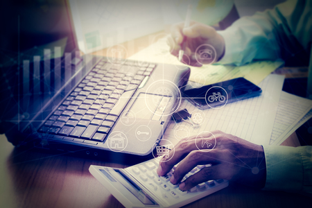 Hands of a business man working on calculator and laptop in office with virtual graphic icon diagram.の写真素材