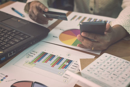 Businesswoman using mobile phone to online payment by credit card with marketing information graph...