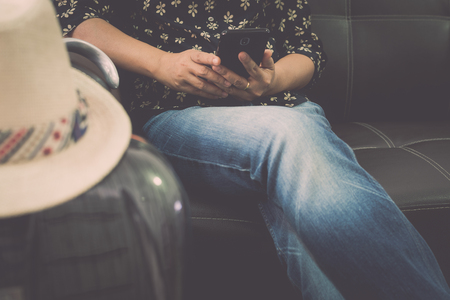 Female traveller is relaxing on leather sofa holding mobile phone at the airport. Travel concept.の写真素材