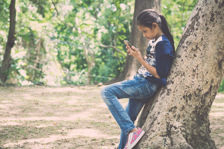 Young girl using mobile phone under big tree in the garden under sunlight.の写真素材