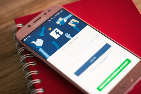 PHUKET, THAILAND - AUGUST 23, 2018 : Facebook social media app logo on log-in, sign-up registration page on Samsung J7 Pro mobile screen with red notebook on wooden table.のeditorial素材