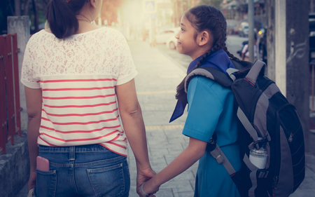 Mother and daughter are walking hand in hand to school under sunlight.の写真素材