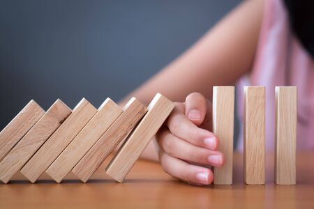 Girl's hand Stopping Falling wooden Dominoes effect from continuous toppled or risk, strategy and successful intervention concept for business and education.の写真素材