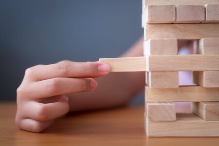 Hand of a girl placing and pulling wooden block on the tower. Alternative risk concept, plan and strategy in business and education.の写真素材