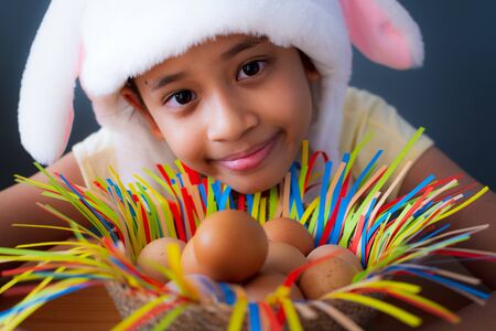 Happy easter! Close up cute girl wearing rabbit hat with chicken eggs in a basket, Easter holiday concept.の写真素材