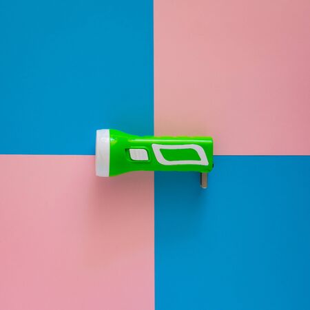 Top view green flashlight on pink and blue paper background.の写真素材