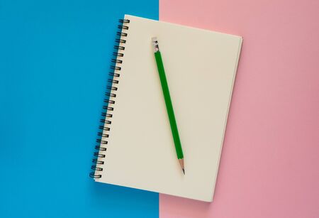 Open notebook with green pencil isolated on pink and blue paper background, Education concept.の写真素材