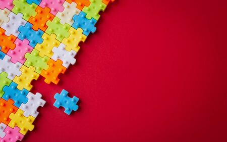 Colors plastic jigsaw puzzle on red paper background, Missing one jigsaw puzzle to complete with copy space, Business strategy teamwork and problem solving concept.の写真素材