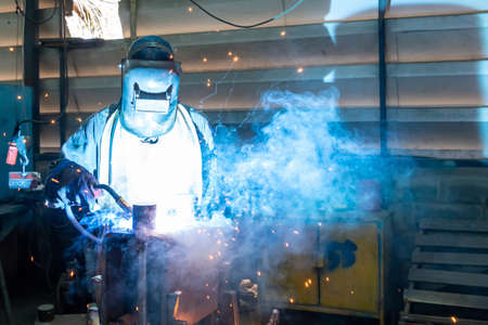man or worker welding metal part at factory with very smoke and sparkle bright right