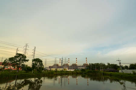 Natural gas electric power plant with smokestack and many pole in chonburi thailand with water reflection and beautiful sky near eveningの写真素材