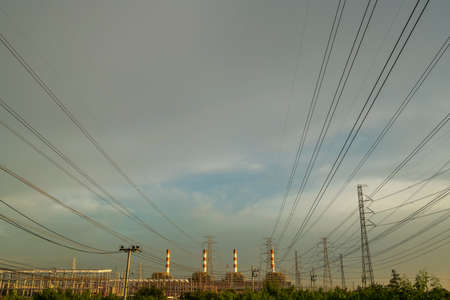 Many high voltage power pole and cable lines with smokestack of power plant in back with beautiful...