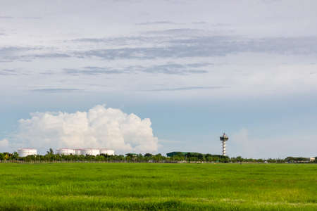 airport control tower for air traffic management with at green field near oil tank on cloudy sky...