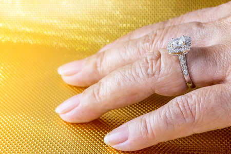 Beautiful and luxury wedding diamond ring worn on woman hand on gold backgroundの写真素材