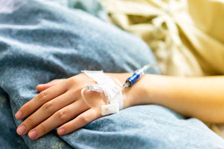 Focus on the hand of a patient in hospital ward on bed during dosing of intravenous salineの写真素材
