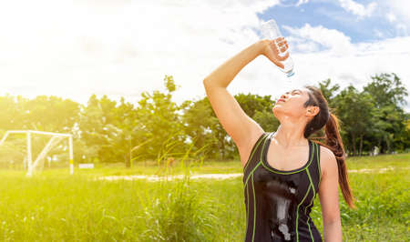 asian young woman pour clean or pure water on face after exercise or running at outdoor sports field