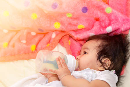 Portrait close up asian cute baby sucking milk form bottle after wake up happily on the bed in room