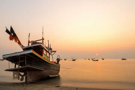 Beautiful seascape sunset with golden sunshine and fishing boat at the beach with copy space (long exposure)の写真素材