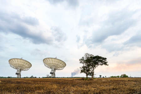 high technology large satellite dish radar or radio telescopes station in meadow or field at countryside and cloudy skyの写真素材