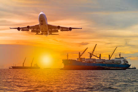 Commercial passenger airplane fly over a large general cargo ship sailing in the sea near the coast and spread the wheel prepare landing to airport in evening while golden sunsetの写真素材