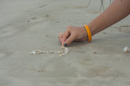 Hand of woman is drawing image on the beach.