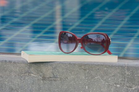 Sun glasses on book with swimming pool background.の写真素材