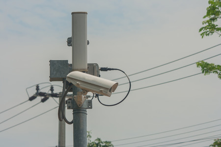 Closed-circuit camera on electric pole and walkway in public park.