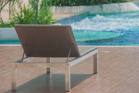 Relaxation Concept : Daybed beside swimming pool on wooden floor with blue green water background.