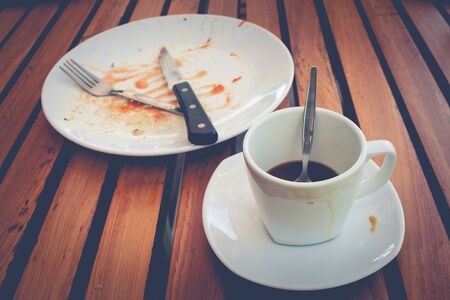 Dirty coffee cup and dish after eat breakfast and drinking coffee with wooden table background. (Autumn filter effect)の写真素材
