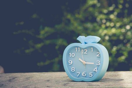 Time Management Concept : Blue alarm clock on concrete floor with green leaves background. (Autumn...
