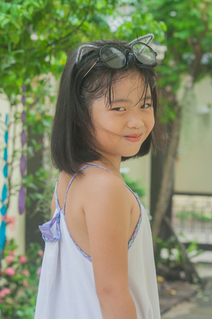 Cute little Asian Chinese girl and her glasses perched on top of her head smiling and happiness in the garden.の写真素材