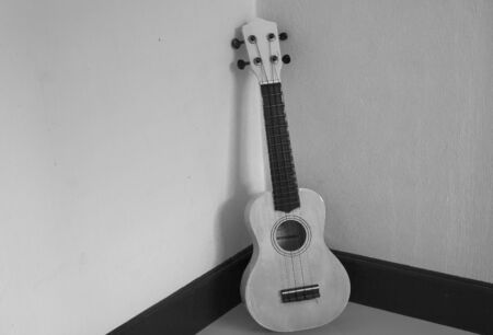 Musical instrument ukulele guitar on gray tile floor at room corner. (Black and White filter effect)